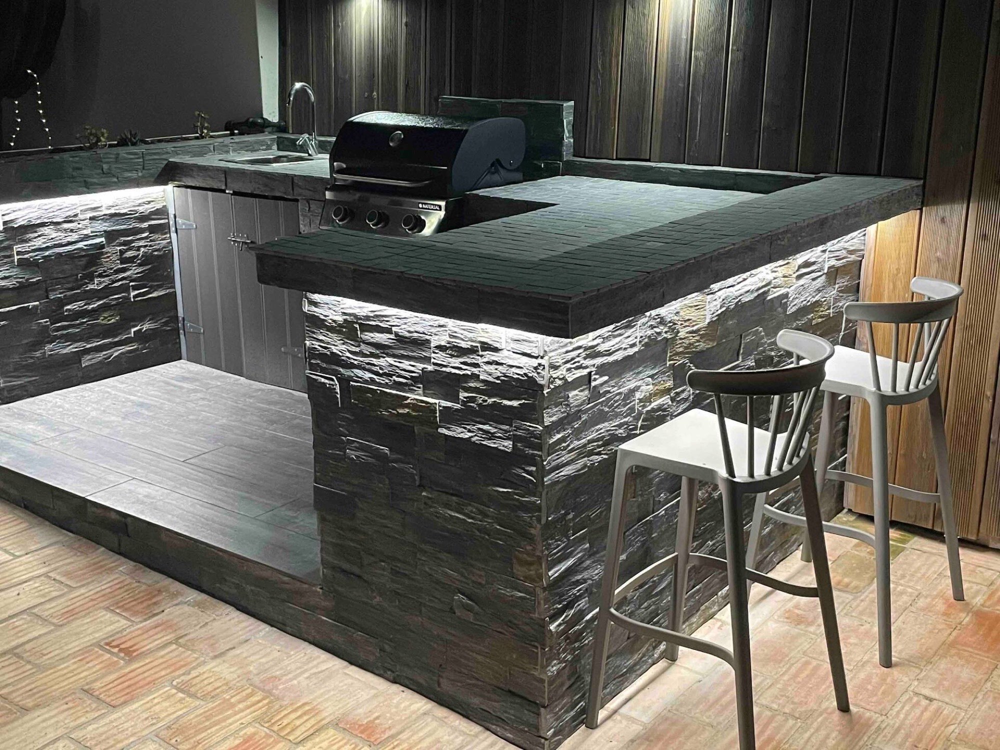 Stone-built outdoor kitchen and bar lit up at night
